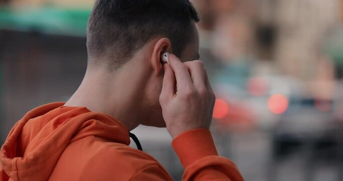A man in orange puts on wireless earphones on the city street, slow motion at 120 fps