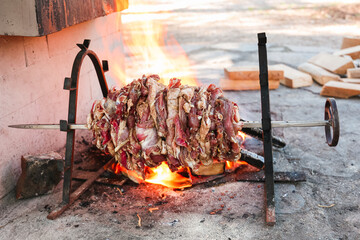 fresh lamb meat on an open fire on a skewer for roasting-jack. daylight, wooden blocks are visible...