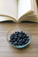 Bowl of blueberries and open book on a table. Selective focus.