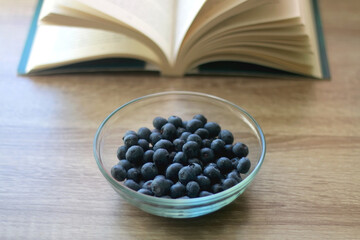 Bowl of blueberries and open book on a table. Selective focus.