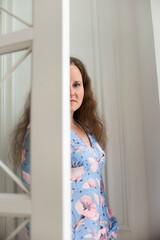 A beautiful woman with curly hair in a blue patterned dress smiles and takes notes in the bright cozy interior of the house
