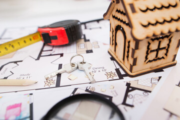 Fototapeta premium wooden toy house, keys with a tape measure and a magnifying glass on the plan of the house.