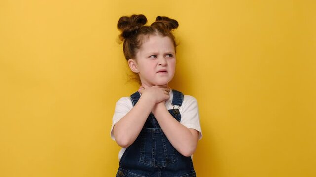 Unhealthy little girl kid touch neck feels discomfort painful feelings hard to swallow, sore throat pain irritation or loss of voice, isolated on yellow studio background. Tonsillitis angina concept