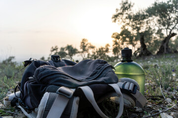 Backpack and water bottle placed in the ground of the countryside against beautiful sunset.