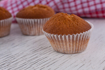 Morning breakfast vanilla muffins in white paper cups on a white wooden cutting board, white background, close-up view 