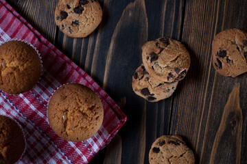 Morning breakfast vanilla muffins in white paper cups on a beautiful towel, close-up, with chocolate cookies. Wooden background.