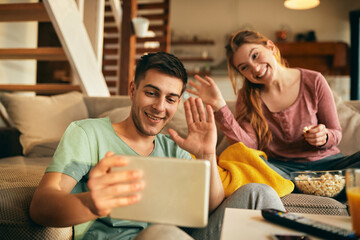 Happy couple waving during video call over touchpad at home.