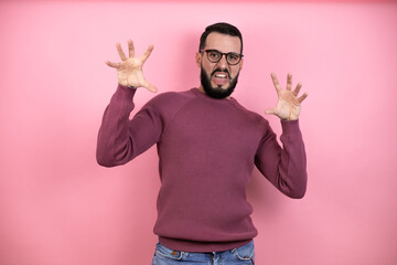 Handsome man wearing glasses and casual clothes over pink background smiling funny doing claw...