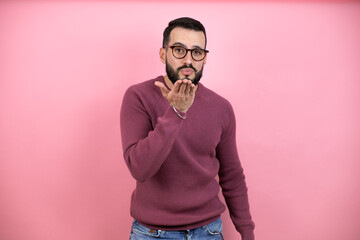 Obraz premium Handsome man wearing glasses and casual clothes over pink background looking at the camera blowing a kiss with hand on air being lovely and sexy. Love expression.