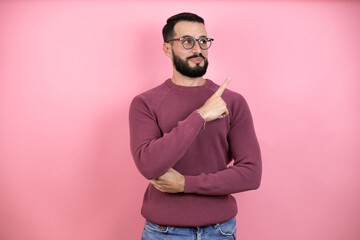 Handsome man wearing glasses and casual clothes over pink background confused and pointing with hand and finger to the side