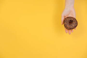 Hand holds a chocolate donut. Copy space. Selling confectionery. Round tasty donuts on a yellow background 