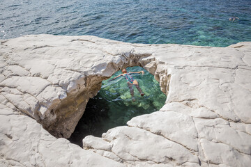 A young girl in a swimsuit lying on the turquoise sea water in a cave. In white rock, hole and sea....