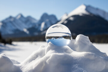 A scenic snow peaked mountain range view inverted inside a lens ball, on a snow bank on a sunny day.