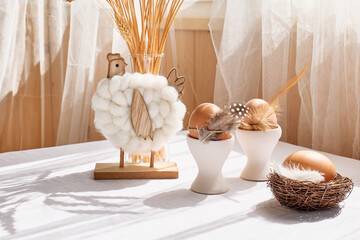 Easter table composition with brown eggs in white ceramic egg cups and wooden easter hens on the table with white tablecloth. Happy Easter. Scandinavian style background