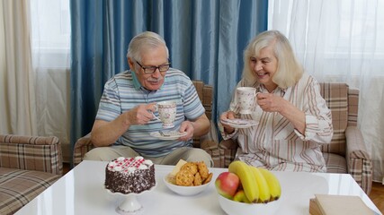 Senior family couple grandfather, grandmother relaxing on cozy sofa enjoying conversation at home