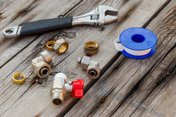 Various plumbing spare parts, sealing tape and adjustable wrench on rustic wooden background