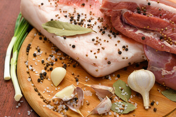 raw pork meat and lard with salt, spices and garlic on a cutting board, dark wooden background