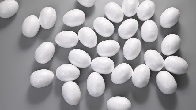Easter. Many eggs roll of the same color, white, roll on a gray background. Top view, stop motion. In the style of minimalism. Easter concept. High quality FullHD footage