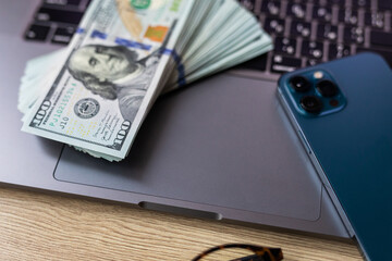 Business concept - laptop, banknotes of us dollars, smart phone and glasses. Top view of the texture of expensive wood. Picture with space for your text.