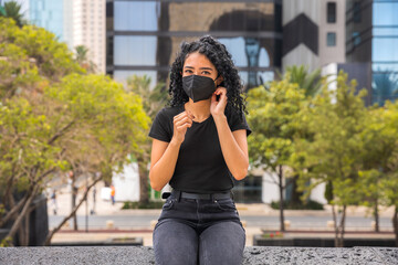 Young woman with curly head putting a black mask on her face