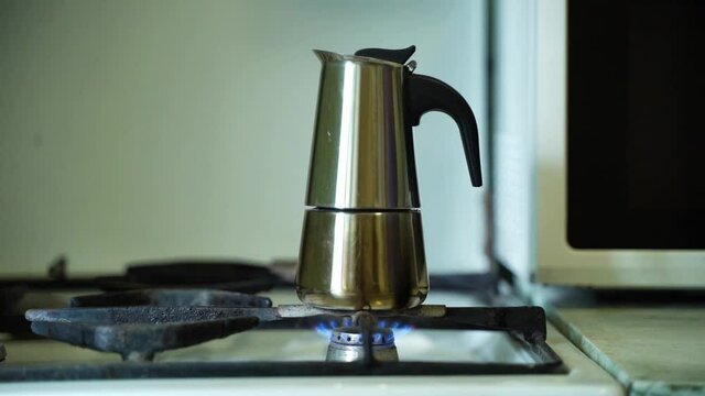 male hand hand with a burning match sets fire to a gas burner with a geyser coffee maker, moka pot. close-up, camera movement from left to right, full HD.