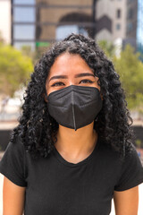 Young woman with curly hair is sitting. He is wearing a black mask