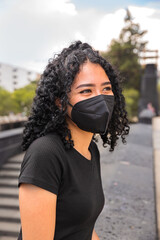 Young woman with curly hair is sitting. He is wearing a black mask