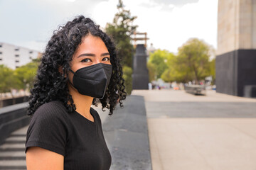 Young woman with curly hair is sitting. He is wearing a black mask