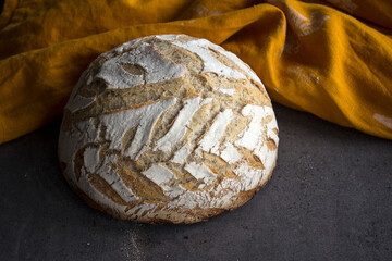 White round bread with leaves pattern on the top. Yellow linen fabric on background. Sourdough bread close up photo. 