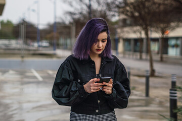 Young woman with purple hair using her cell phone and walking