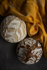 Two round freshly baked breads on yellow linen fabric background. Artisan bread top view photo. 