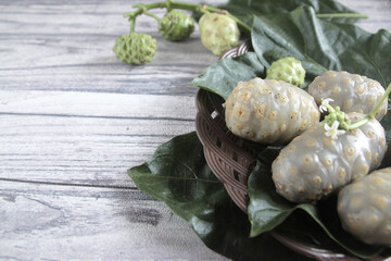 Noni fruit, freshly plucked on a plastic plate and leaves, is served on a wooden table