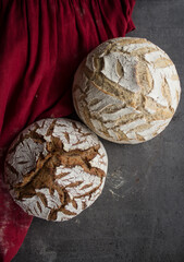 Two round sourdough breads on red linen towel. Top view photo of beautifully scored artisan bread. Crusty loaf texture. Gray background with copy space. Healthy eating concept. 