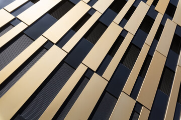 Modern, abstract facade with gold and black elements from oblique angle with sun reflection as...