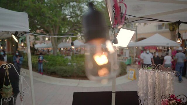 CLOSE UP OF A LIGHT BULB ILUMINATING A FLEE MARKET WHERE PEOPLE WERE MASKS