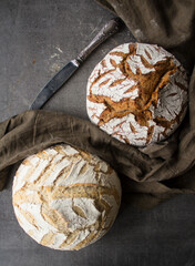 Two breads on dark linen fabric. Grey textured background with copy space. Home bakery. Artisan bread scoring ideas. 