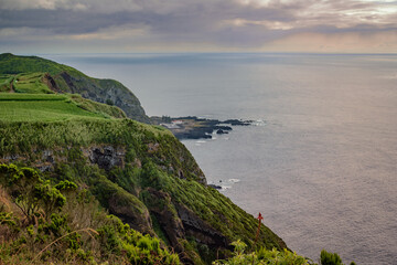 Fototapeta premium Cliff with vegetation and green field overlooking the hot sea springs of Ponta da Ferraria in lava fajã at sunset, São Miguel - Azores PORTUGAL