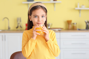 Cute little girl drinking orange juice in kitchen