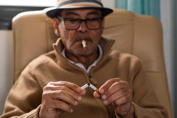 Senior man with a plastic cigar in his mouth, looking thoughtful at a broken cigar he is holding in his hands