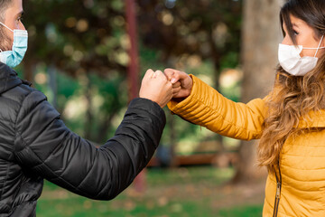 Young friends greeting each other bumping fists with mask in park