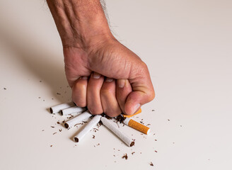 Fist of a man hitting a pile of broken cigarettes on a white table