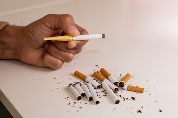 Hand of a man holding a plastic cigarette to quit smoking, next to a pile of broken cigarettes