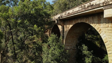 Drone images of the Knapsack Bridge, an old sandstone arch bridge, on a sunny spring morning surrounded by green eucalyptus trees.