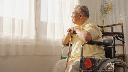 Portrait depressed lonely elderly man with wooden cane looking at windows, frustrated mature male folded hands on walking stick, sitting on wheelchair alone, loneliness and solitude, Care, Retirement.