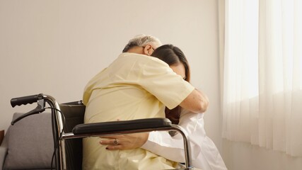Asian young lady in white lab coat taking care of patient. Thai woman doctor hugs the old man patient lovingly She encouraged the old man to smile and be happy. They looking at each other and smiling