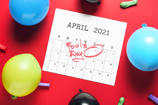 Calendar with marked date of April Fool's Day and party decor on color background