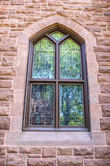 Leaded gothic window in rock building on University campus reflecting trees and nature.