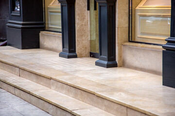 beige marble threshold with steps at entrance to glass door of expensive store with black decorative columns made of wood and transparent windows showcases on facade of building side view, nobody.