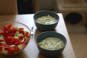 Two bowls of pasta with zucchini sauce and a bowl of cucumber and tomato salad. Selective focus.