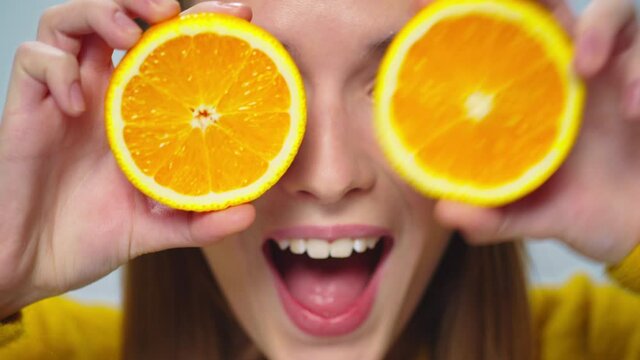 Closeup young pretty woman making faces with two orange slices indoors.